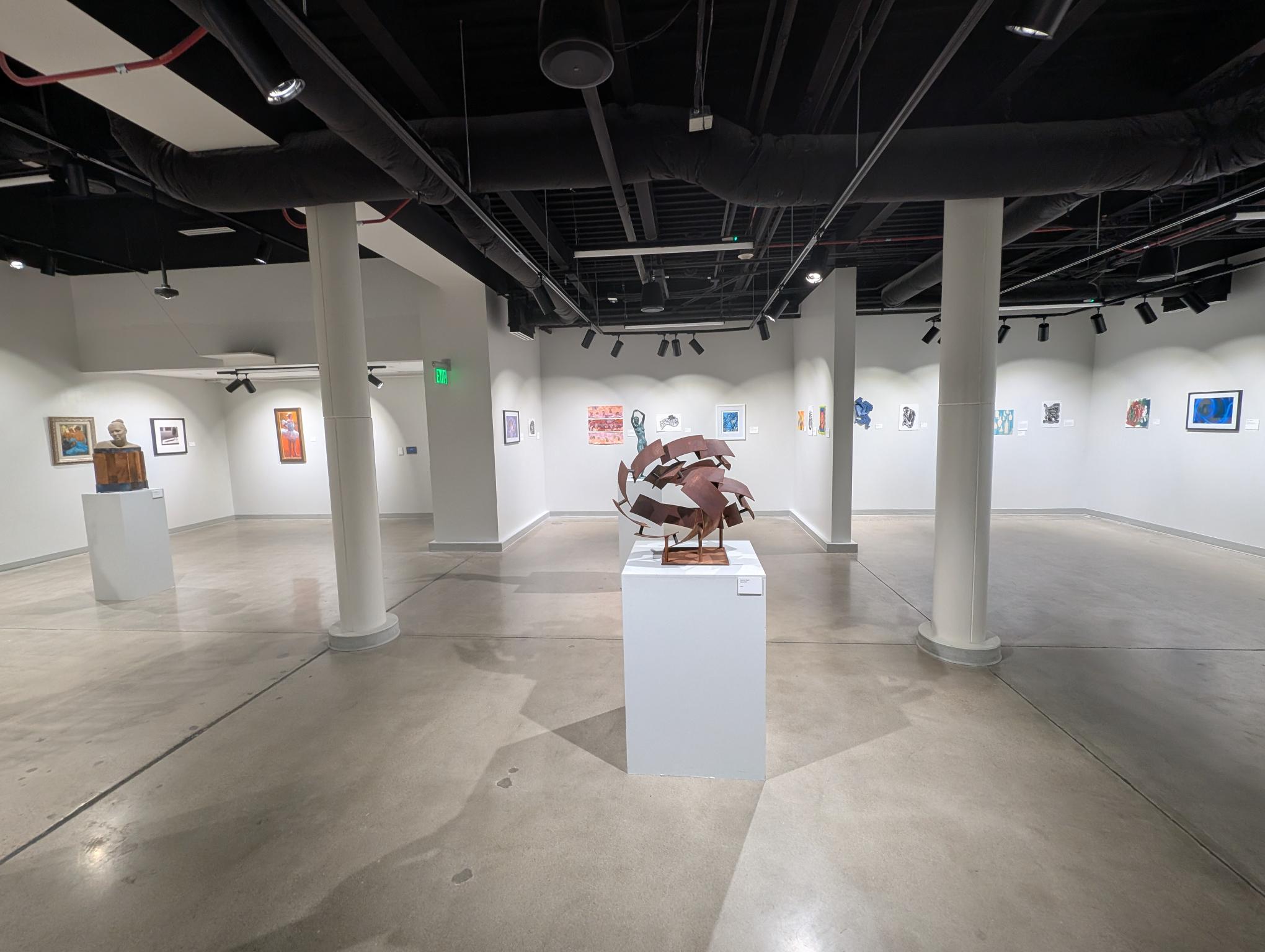 A circular, metal sculpture sitting in the middle of a white gallery space