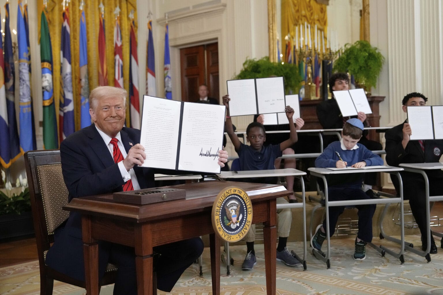 President Trump holding signed executive order beside young children holding copies in the East Room of the White House